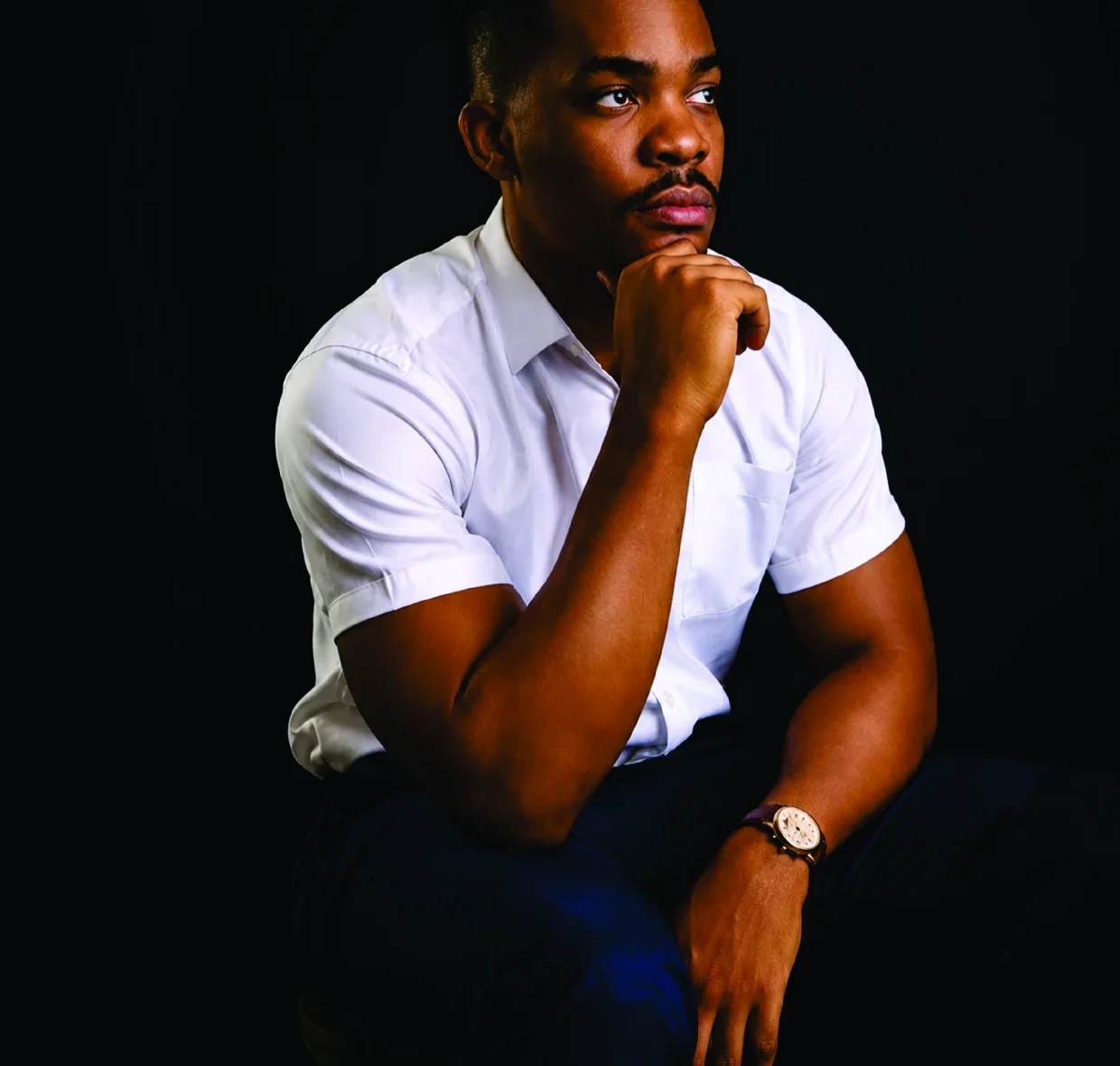 Kennedy Ekezie seated, chin resting on his hand, in a white shirt