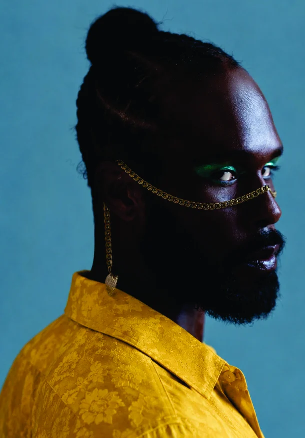 Profile of a man with a gold face chain and green eye make-up