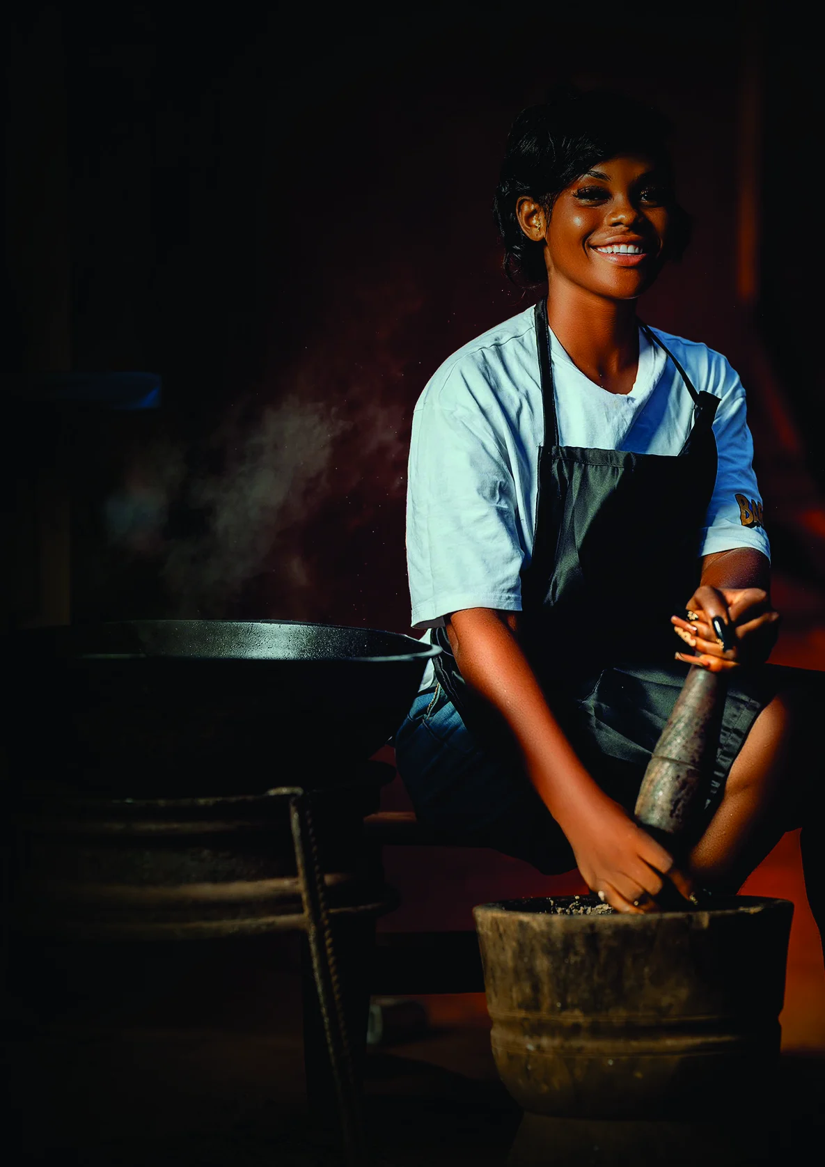Jideobi Chiamaka Favour smiling as she pounds beans at a wooden mortar