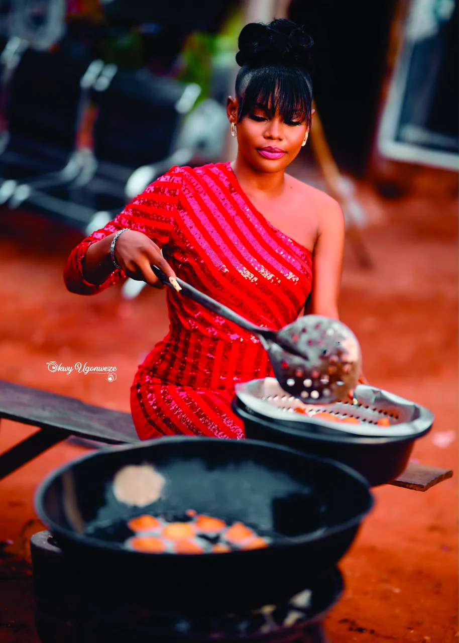 Chiamaka frying akara in a red one-shoulder sequin dress