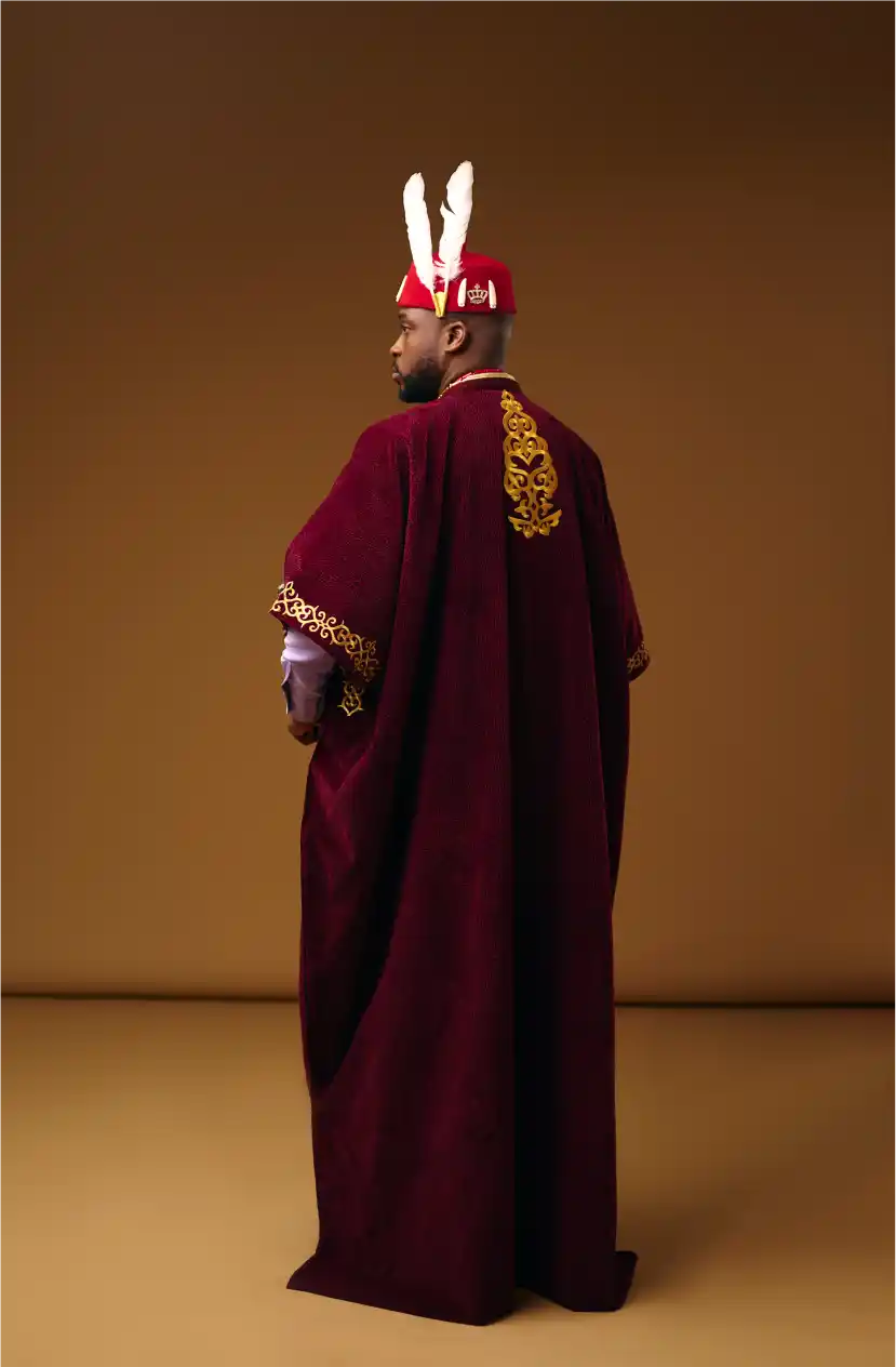 Man in feathered royal headdress and ornate cape, seen from behind