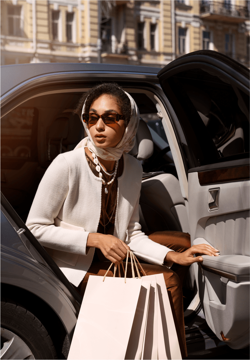 Elegant woman in white headscarf carrying luxury shopping bags beside a car