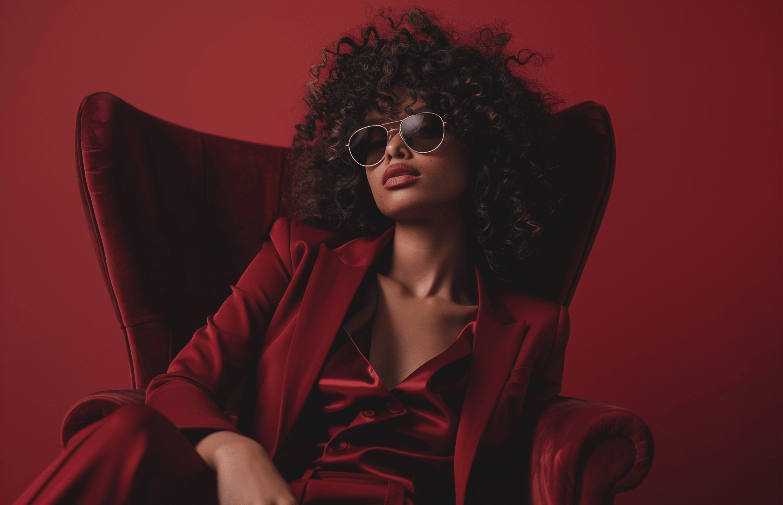 Editorial portrait — woman in deep red satin suit seated in a velvet chair